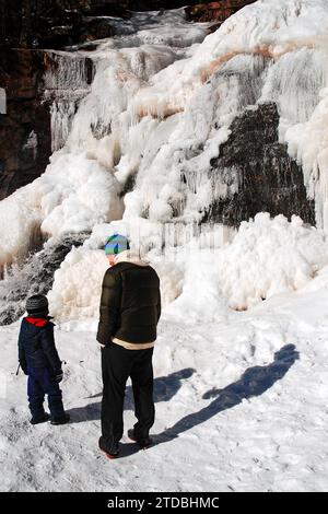 Un père et son fils à une randonnée vers une chute d'eau gelée par un froid glacial jour d'hiver dans un parc d'État à Kaaterskill Falls Banque D'Images