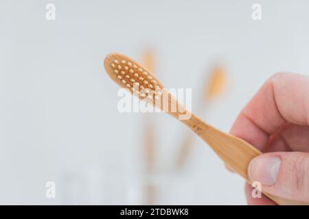 Bambou brosse à dents.nettoyage des dents.brosse à dents à la main sous l'eau du robinet dans la salle de bain. Main prend une brosse à dents d'une tasse en verre transparent sur l'évier dans un Banque D'Images