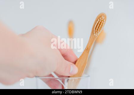 Brosse à dents.nettoyage des dents.brosse à dents à la main sous l'eau du robinet dans la salle de bain. Main prend une brosse à dents d'une tasse en verre transparent sur l'évier dans un Banque D'Images