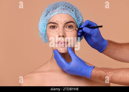 Médecin dessinant des marques sur le visage de la femme pour l'opération de chirurgie esthétique sur fond beige Banque D'Images