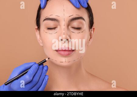 Médecin dessinant des marques sur le visage de la femme pour l'opération de chirurgie esthétique sur fond beige Banque D'Images