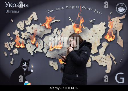 Kiev, Ukraine. 16 décembre 2023. Une femme marche près d'une maquette d'un timbre-poste avec l'inscription "l'Empire du mal doit tomber" et brûle les terres russes dans le centre de Kiev. (Photo Oleksii Chumachenko/SOPA Images/Sipa USA) crédit : SIPA USA/Alamy Live News Banque D'Images