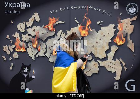 Kiev, Ukraine. 16 décembre 2023. Une femme avec un drapeau ukrainien marche près d'une maquette d'un timbre-poste avec l'inscription "l'Empire du mal doit tomber" et brûle les terres russes dans le centre de Kiev. (Photo Oleksii Chumachenko/SOPA Images/Sipa USA) crédit : SIPA USA/Alamy Live News Banque D'Images