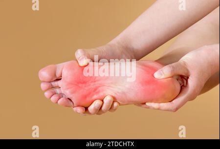 Une femme souffrant de douleurs plantaires sévères masse son pied, isolé sur fond beige (marqué en rouge) Banque D'Images