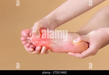 Une femme souffrant de douleurs plantaires sévères masse son pied, isolé sur fond beige (marqué en rouge) Banque D'Images