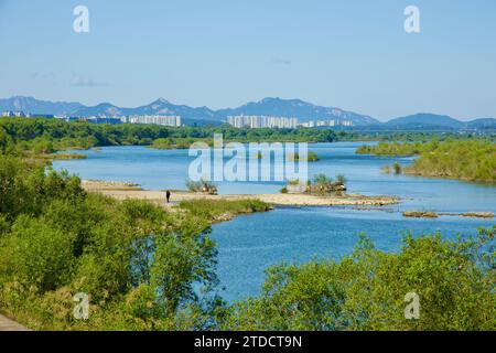 Hanam City, Corée du Sud - 1 octobre 2023 : une scène tranquille de la rivière Han, avec un banc de sable et une figure lointaine, encadrée par des montagnes et du blanc Banque D'Images