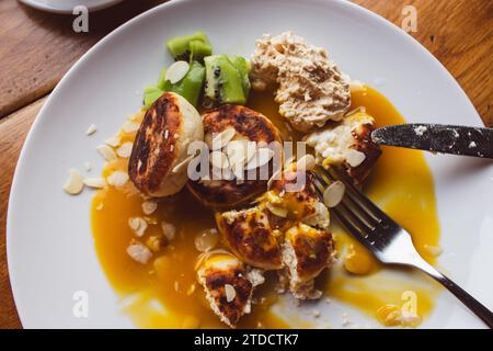 Cheesecakes au sirop de mangue et flocons d'amande sur plaque blanche. Petit déjeuner sucré au café. Syrnik avec chalet et avocat. Crêpes au fromage avec sirop. Banque D'Images