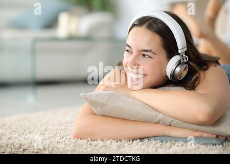 Femme heureuse écoutant de la musique avec un casque couché sur un tapis à la maison Banque D'Images