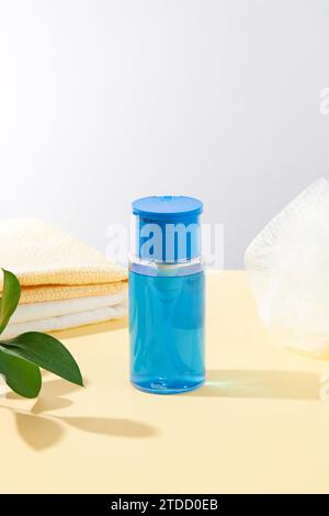 Gros plan d'une bouteille bleue transparente de démaquillant se détachant sur un fond pastel. Concept de nettoyage de la peau. Maquette cosmétique pour la publicité. Banque D'Images