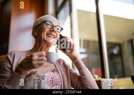 Femme mature est assise dans le café et relaxant. Elle parle au téléphone. Banque D'Images