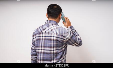 Vue arrière du jeune homme asiatique répondant à l'appel de téléphone portable sur fond blanc. prise de vue en studio Banque D'Images