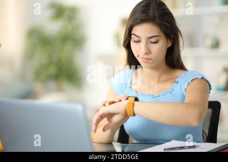 Femme suspecte vérifiant le contenu de smartwatch assis à la maison Banque D'Images