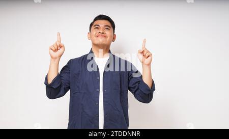 Souriant heureux jeune homme asiatique pointant les deux mains vers le haut sur fond blanc. prise de vue en studio Banque D'Images