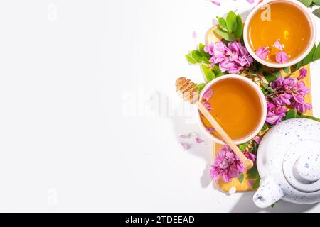 Boisson de santé biologique à base de plantes. Thé vert fleur d'acacia, dans des tasses blanches, avec une théière, sur une table blanche, avec espace de copie et fleur d'acacia en fleurs Banque D'Images