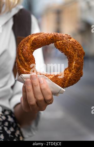 Femme tient un gros plan d'un bagel turc traditionnel simit dans la rue. Restauration rapide turque. Photo verticale Banque D'Images