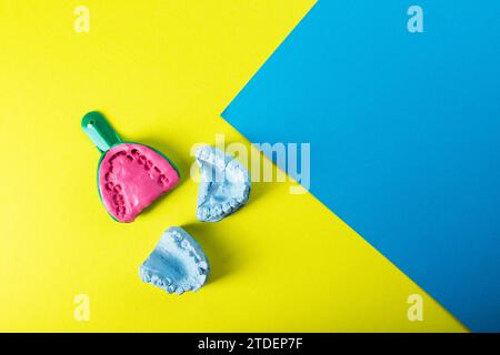 Plateau dentaire avec masse plastique alginate et mâchoire en plâtre bleu du patient sur fond jaune-bleu. Le concept de fabrication de fausses mâchoires, denta Banque D'Images