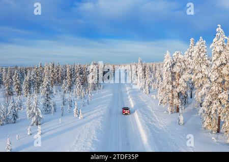 Vue drone d'une voiture roulant sur une route vide et gelée dans le paysage blanc de la Laponie suédoise, la Suède, la Scandinavie, l'Europe Banque D'Images