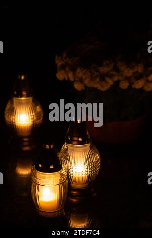 Cliché de nuit des flammes des bougies de cimetière en verre debout sur les pierres tombales. Le tir a été pris pendant la Toussaint, le 1 novembre. Banque D'Images