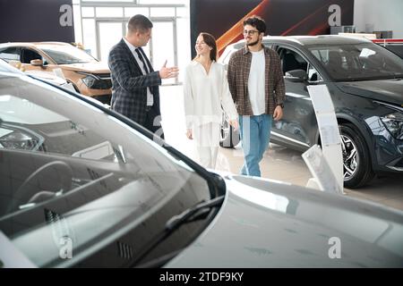 Jeune homme de vente parlant avec des clients homme et femme aide à choisir l'automobile Banque D'Images