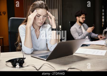 Jeune femme d'affaires épuisée se sentant mal à la tête pendant le travail sur ordinateur portable Banque D'Images