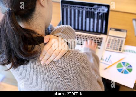 Une femme assise devant un ordinateur portable et travaillant tient son mal au cou Banque D'Images