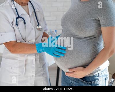 Femme enceinte consultant un médecin. Gynécologue caucasienne âgée tient les mains sur le ventre d'une patiente enceinte. Banque D'Images