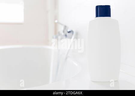 Bouteille blanche de shampooing debout sur une baignoire dans une salle de bain lumineuse - copie espace sur la bouteille Banque D'Images