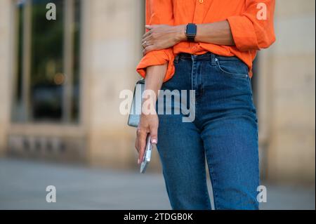 Femme méconnaissable debout à l'extérieur avec smartphone dans les mains. Banque D'Images