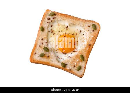 Œuf frit en forme de coeur avec pain grillé aux graines de sésame, graines de lin et graines de citrouille sur une assiette noire sur fond de béton foncé Banque D'Images