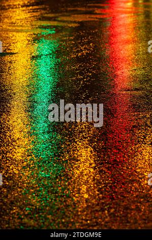 Route asphaltée humide abstraite illuminée de couleur la nuit par des feux arrière de voiture rouges et des feux de signalisation. Banque D'Images