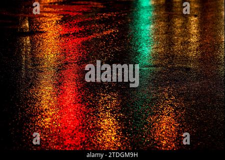 Route asphaltée humide abstraite illuminée de couleur la nuit par des feux arrière de voiture rouges et des feux de signalisation. Banque D'Images