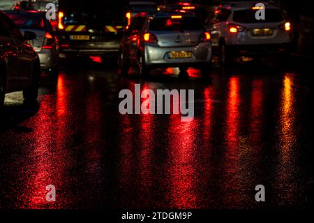 Route asphaltée humide abstraite illuminée de couleur la nuit par des feux arrière de voiture rouges et des feux de signalisation. Banque D'Images