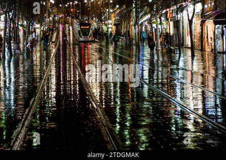 Rendu abstrait du trottoir lisse et des voies du rail léger de Jérusalem illuminé par une lumière artificielle lumineuse et colorée sur un NIG hivernal pluvieux Banque D'Images