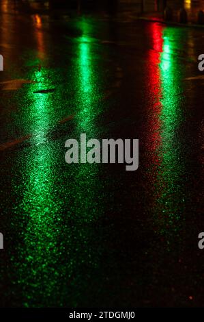 Route asphaltée humide abstraite illuminée de couleur la nuit par des feux arrière de voiture rouges et des feux de signalisation. Banque D'Images