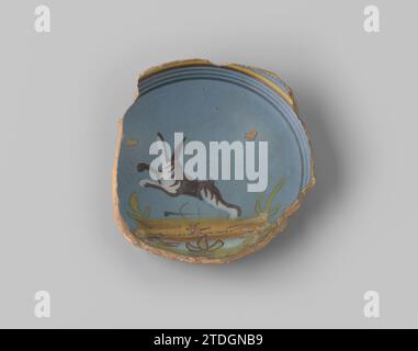 Sharp of ross -Baking faïence, avec anneau de support, avec glaçure bleue à l'avant, sur laquelle une représentation d'un saut brun -lièvre blanc dans un paysage en vert, bleu et jaune, avec quelques rayures autour de l'ensemble, anonyme, 1600 - 1650 Nord des pays-Bas faïence. Faïence majolique du nord des pays-Bas glacés. glaçage majolique Banque D'Images