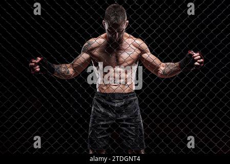 Image dramatique d'un combattant d'arts martiaux mixtes debout dans une cage octogonale. Le concept de sport, boxe, arts martiaux Banque D'Images