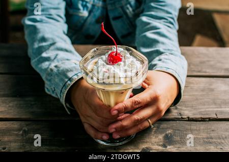 Main femelle tenant le milkshake de cerise sur la table en bois. Personne tenant un smoothie aux cerises sur une table en bois Banque D'Images
