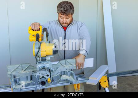 À l'aide d'une scie à découper, l'opérateur découpe le moulage de base en bois à l'aide d'une scie à découper Banque D'Images