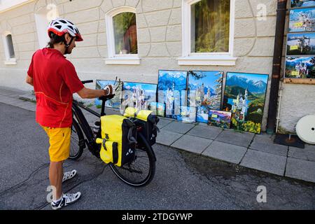 Cycliste regardant des cartes postales kitsch et des peintures devant le château de Hohenschwangau, haute-Bavière, Bavière, Allemagne Banque D'Images