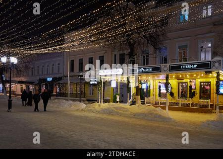 Ryazan, Russie - 16 décembre 2023 : rue du soir enneigée avec vitrines brillantes et gens qui marchent Banque D'Images