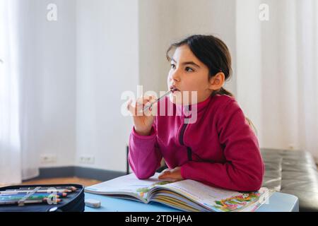 portrait d'une fille réfléchie assise au bureau faisant ses devoirs Banque D'Images