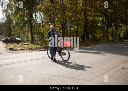 Un homme traverse la route avec un vélo. Vieil homme à vélo marchant à travers l'autoroute. Homme âgé en automne. Pensionné dans la ville . Banque D'Images