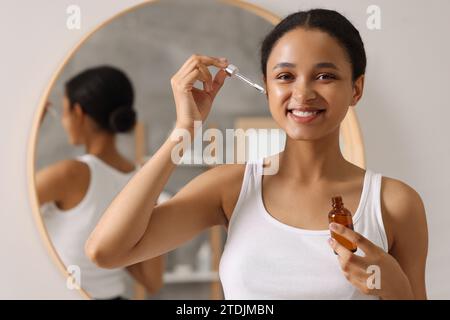 Femme souriante appliquant du sérum sur son visage dans la salle de bain Banque D'Images