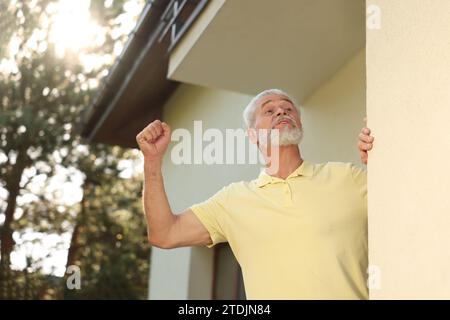 Homme âgé en colère montrant le poing près de la maison, vue à angle bas. Voisin ennuyeux Banque D'Images