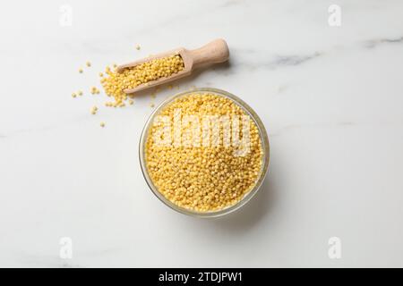 Gruaux de millet dans un bol et pelle sur une table en marbre blanc, pose à plat Banque D'Images