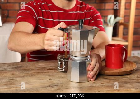 Préparer du café. Homme avec pot de moka à la table en bois à l'intérieur, closeup Banque D'Images