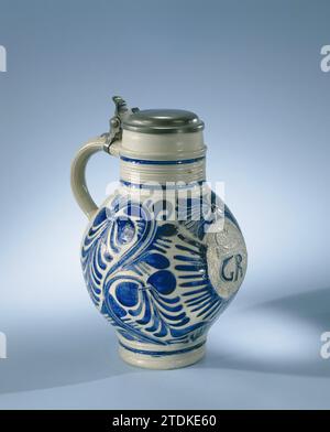 Carafe avec le monogramme 'GR' et feuillets, anonyme, 1724 carafe en grès sur une base haute avec un corps sphérique et un col large et court. L'oreille en forme de C est attachée au cou et au ventre. Quelques lignes et profils sur le cou et le pied. Partiellement recouvert de bleu cobalt. Sur le devant de l'abdomen en relief un monogramme imprimé et imposé 'gr' (George Rex, ou roi George d'Angleterre) en médaillon avec les inscriptions 'HW', '1724', une couronne et une tête d'ange ailée. Le médaillon est entouré de vignes à feuilles. Quelques lignes bleues sur le cou et le pied. Un cadre en étain avec couvercle est fixé à l'oreille. Banque D'Images