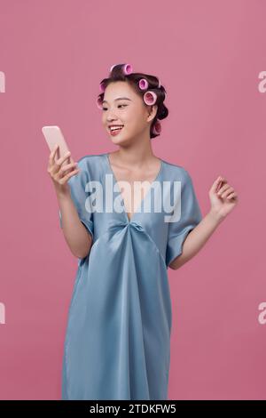 Portrait d'une femme attirante focalisée et joyeuse portant des bigoudis à l'aide d'un support smm Banque D'Images