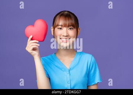 Femme souriante tenant le coeur rouge sur fond violet Banque D'Images