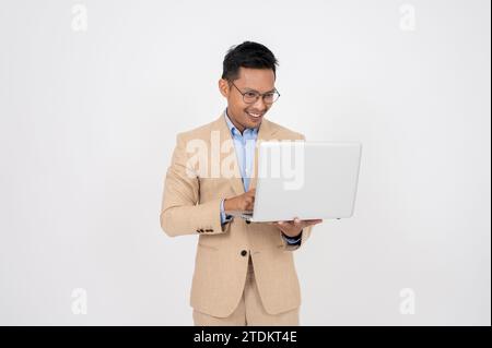 Un bel homme d'affaires asiatique intelligent utilise son ordinateur portable tout en se tenant debout sur un fond blanc isolé. défilement sur le site web, recherche infor Banque D'Images